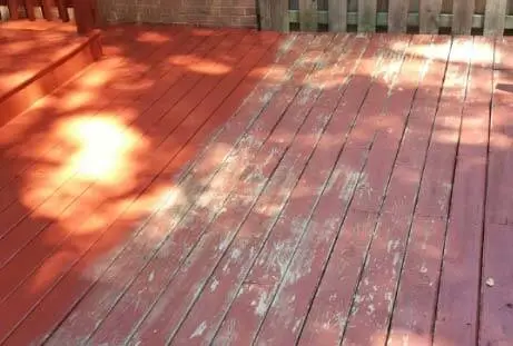A wooden deck with areas of worn, faded red paint, partially shaded by overhanging trees.