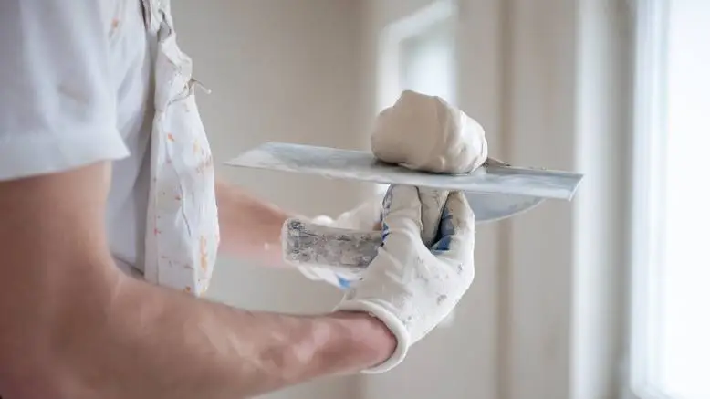 Person wearing a white shirt and gloves holds a plastering trowel with a mound of plaster. painting companies