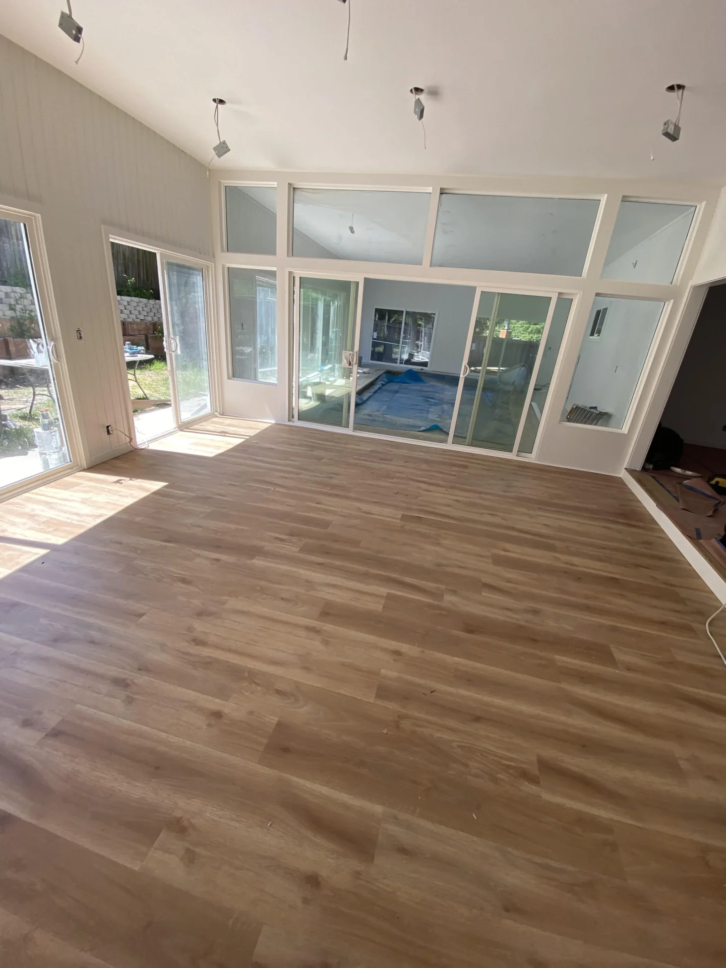 A spacious room with large windows and wooden flooring. The windows offer a view of an indoor pool area. Light fixtures are installed on the ceiling. The room is well-lit with natural light.