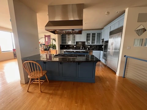 All-Pro-Painting-Services-9 - All-Pro Painting Services A modern building painters kitchen with a central island, black granite countertops, blue cabinetry, stainless steel appliances, and a wooden chair. The floor is wooden and there's a window in the background.