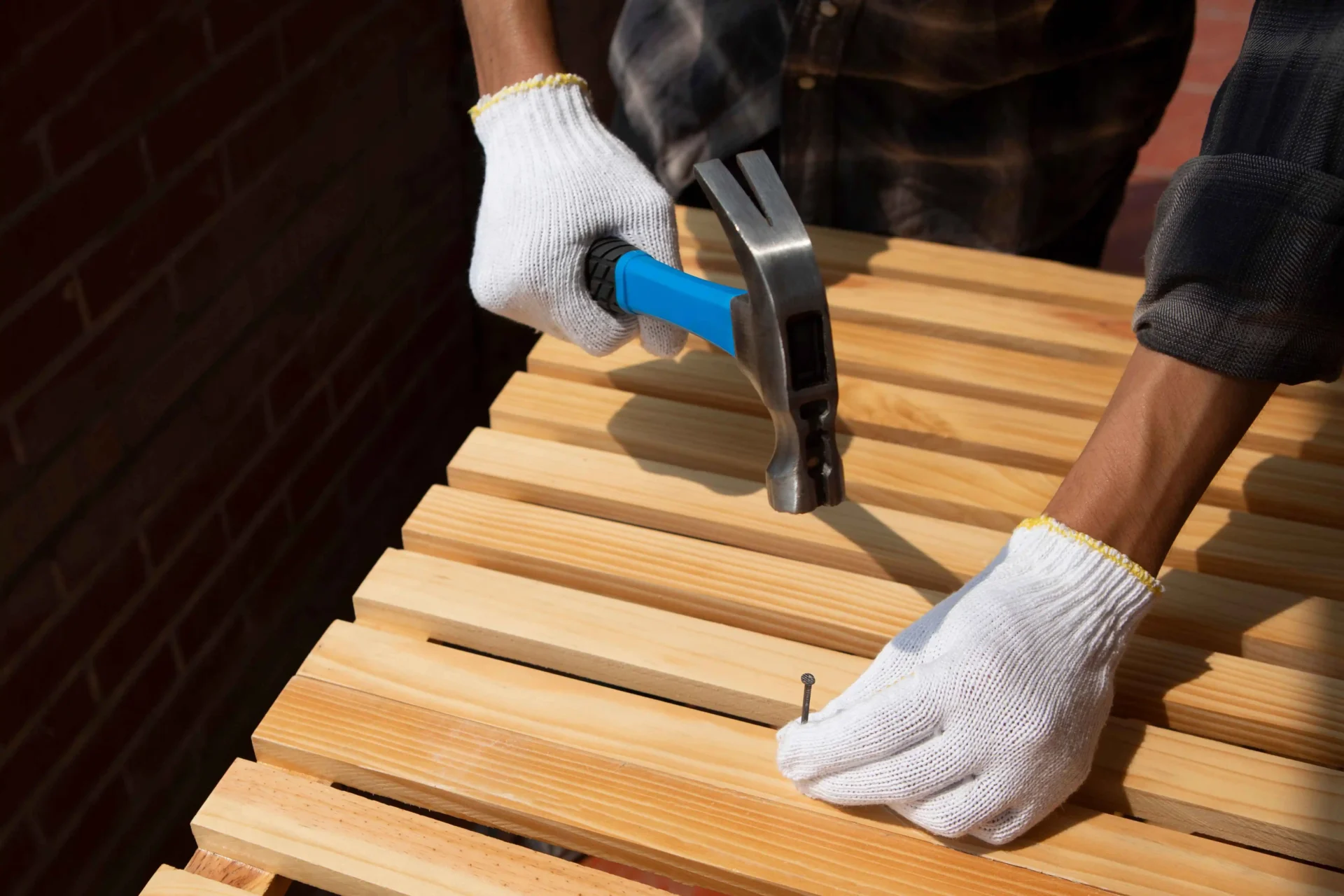 A person wearing white gloves uses a hammer to drive a nail into a wooden slatted surface. exterior restoration
