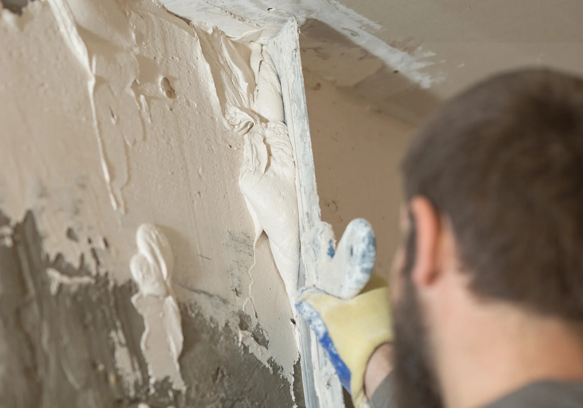 A person applies plaster on a wall using a trowel, focusing on a corner area.